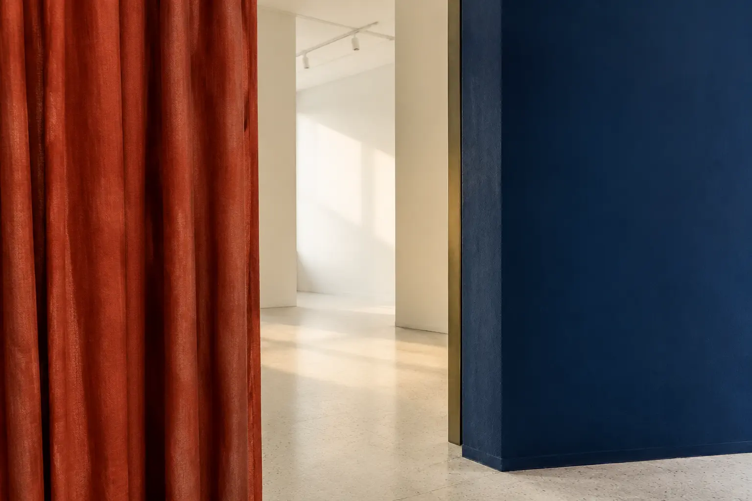 Coral curtain and cobalt wall framing the entrance to a bright cream gallery