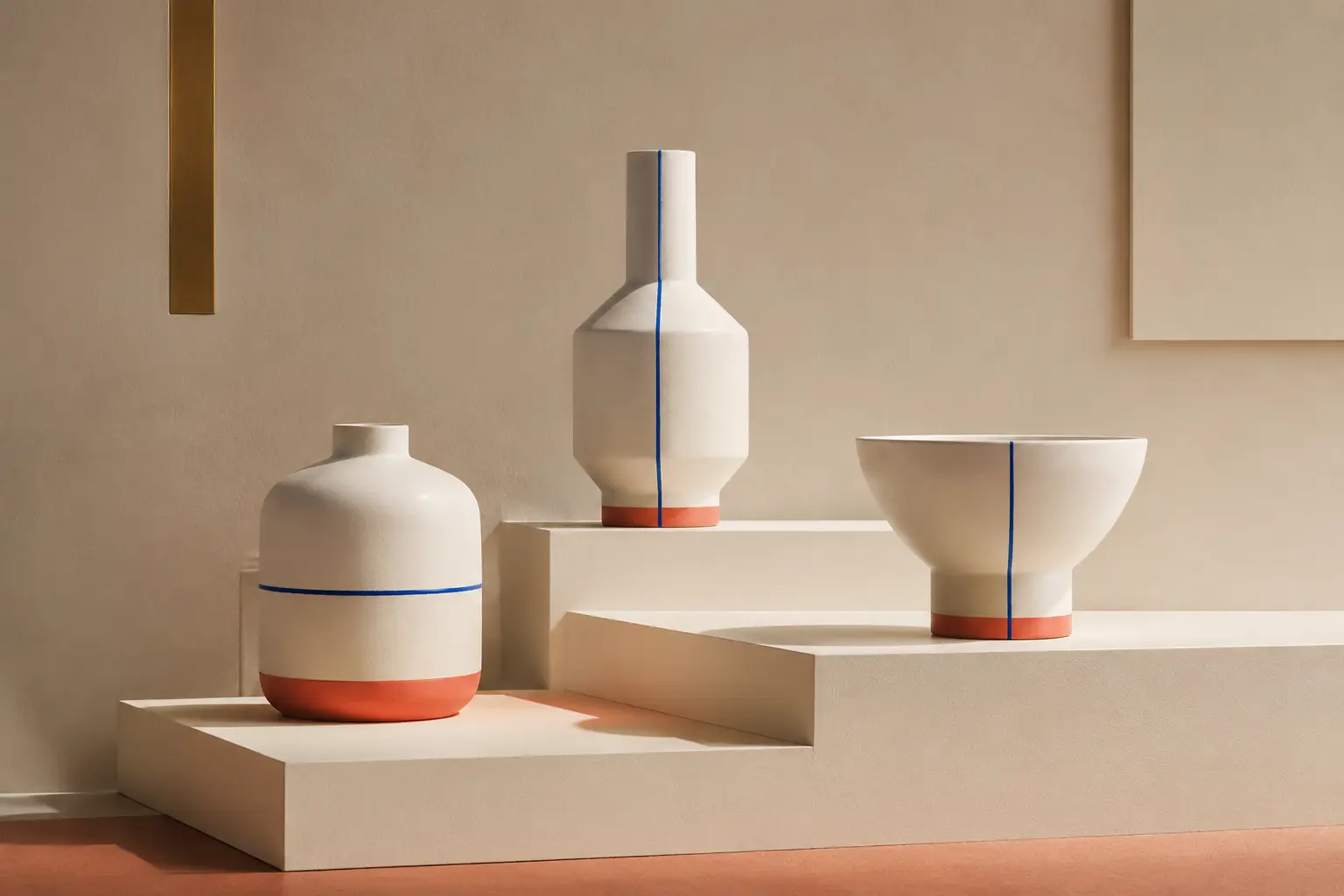 Three distinct cream ceramic forms with cobalt lines and coral bases on stepped plinths